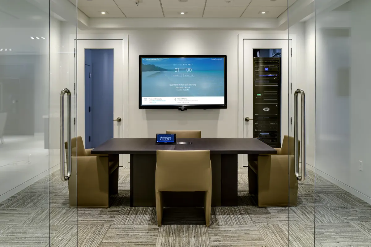 Glass-walled conference room with a wall-mounted display and control panel